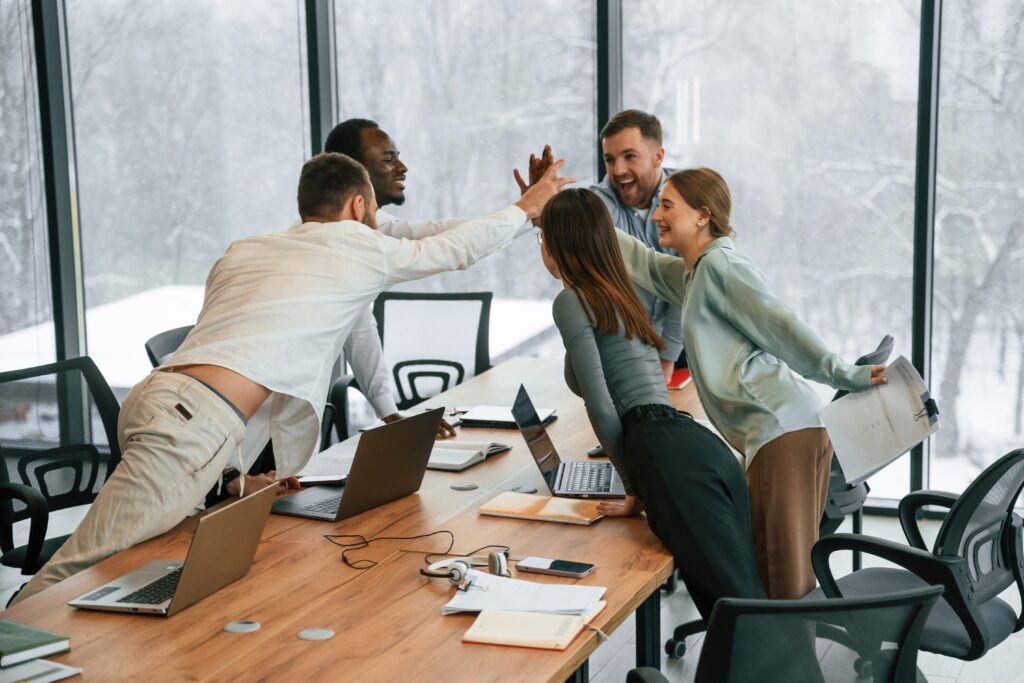 Celebrating success, giving high five. Team of office workers are together indoors.