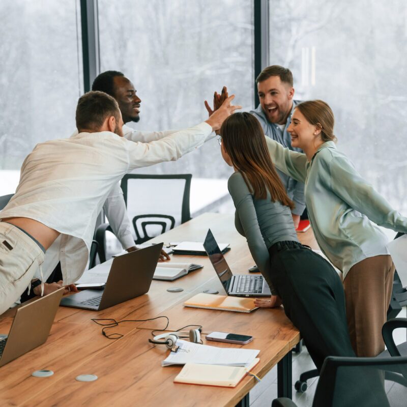 Celebrating success, giving high five. Team of office workers are together indoors.